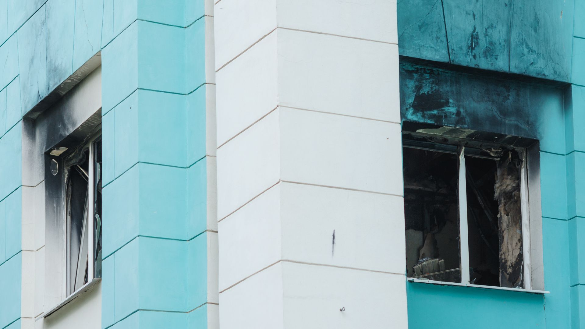 A blue and white building with a broken window and smoke coming out of it.