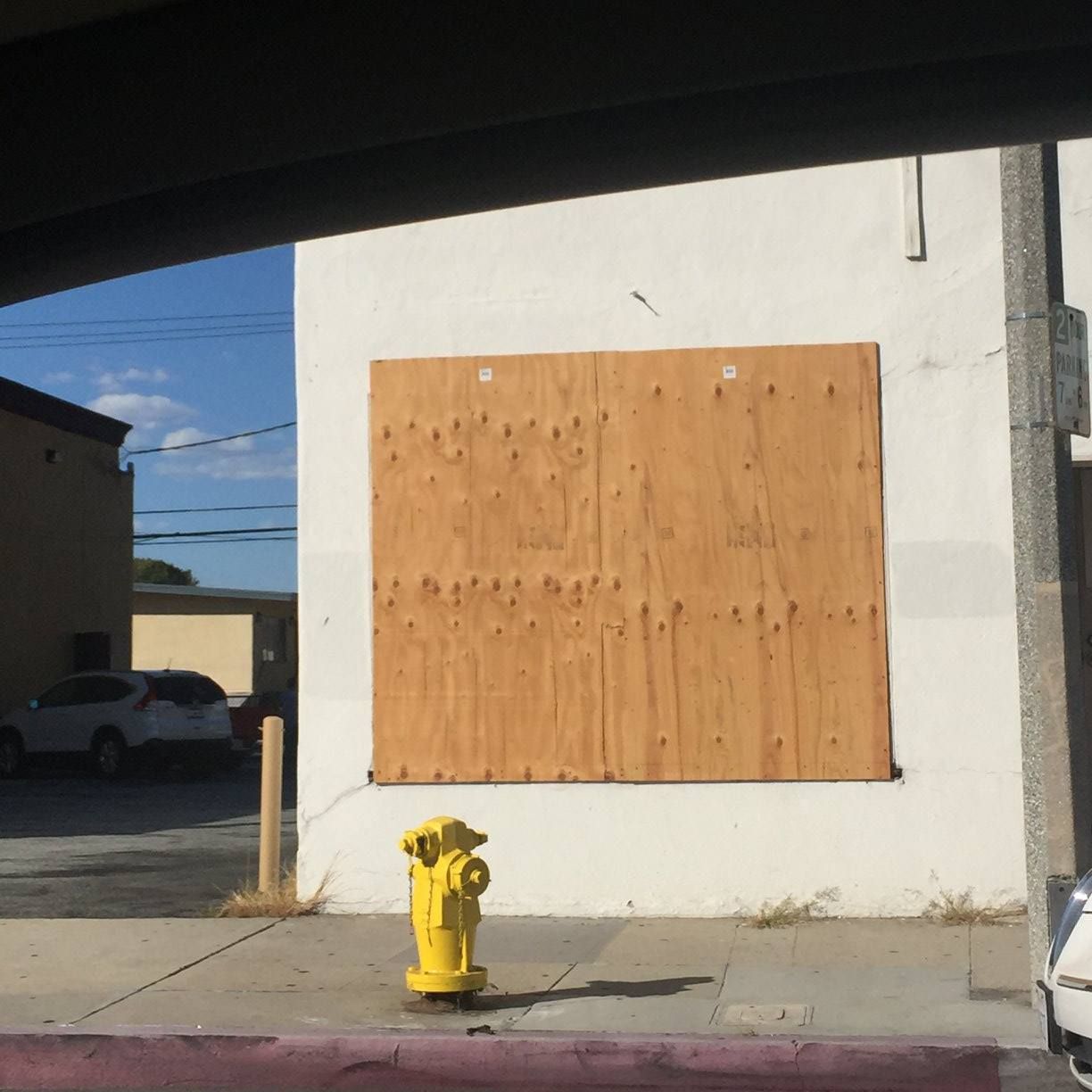A yellow fire hydrant is in front of a building with a boarded up window