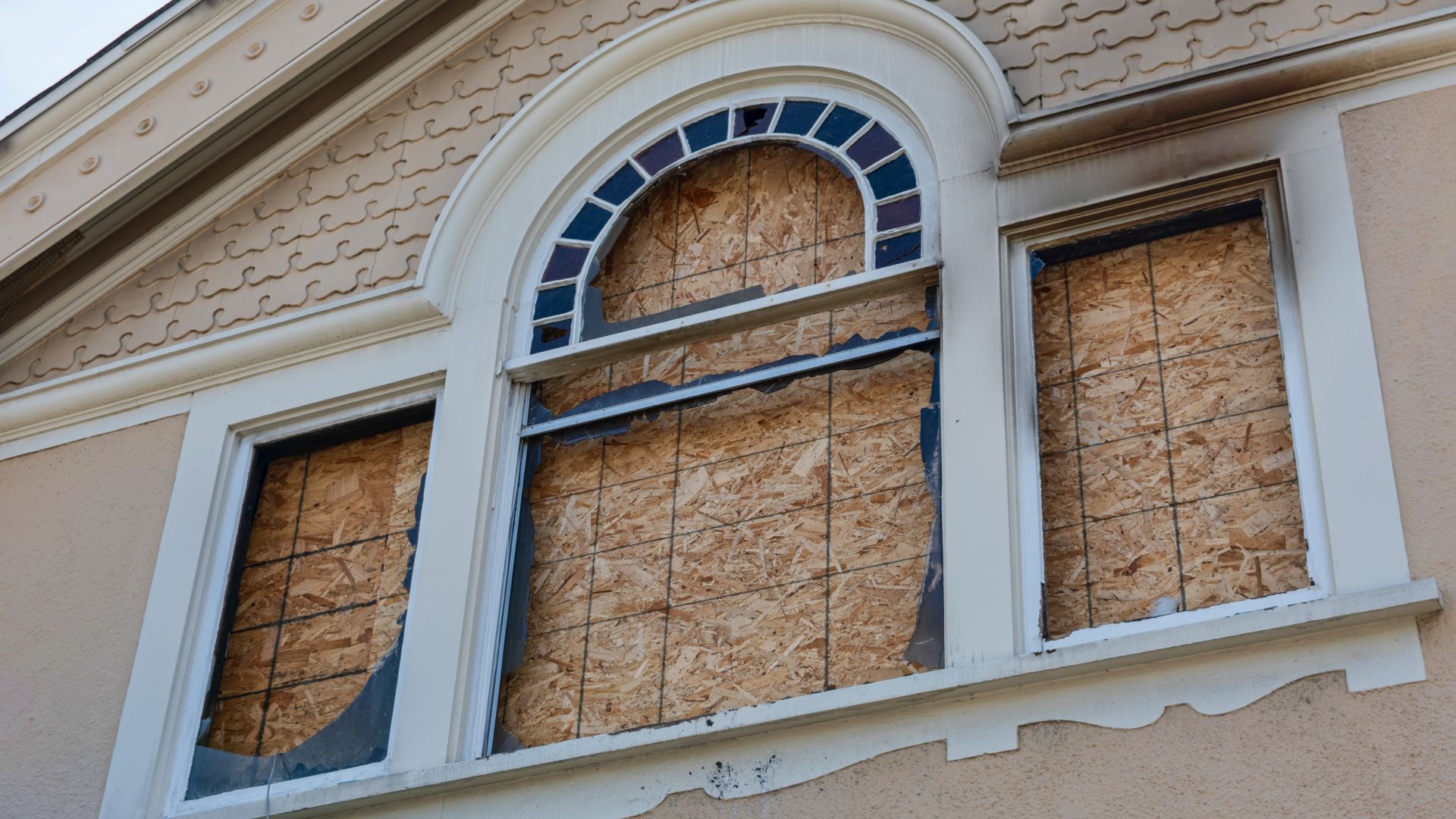 The windows of a building are boarded up with plywood.