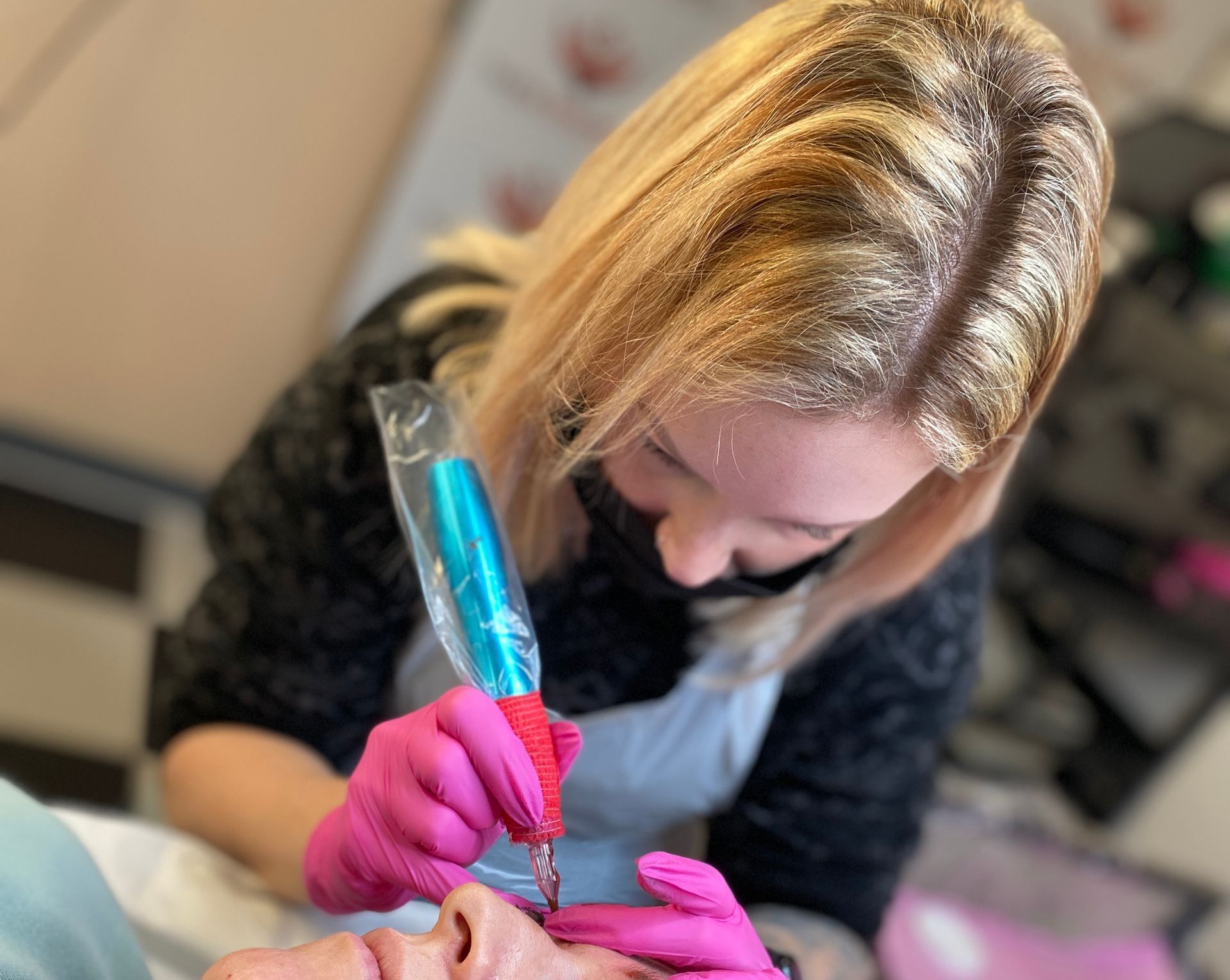 A woman in pink gloves is getting a tattoo on a man 's face.