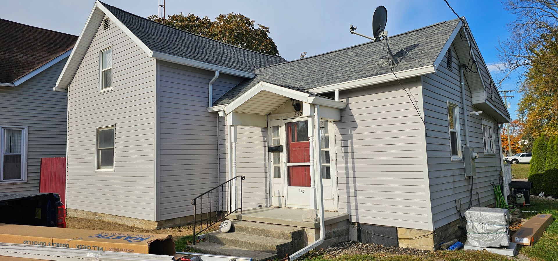 Two-story, light gray house with a red front door and a small porch. Blue sky in the background.
