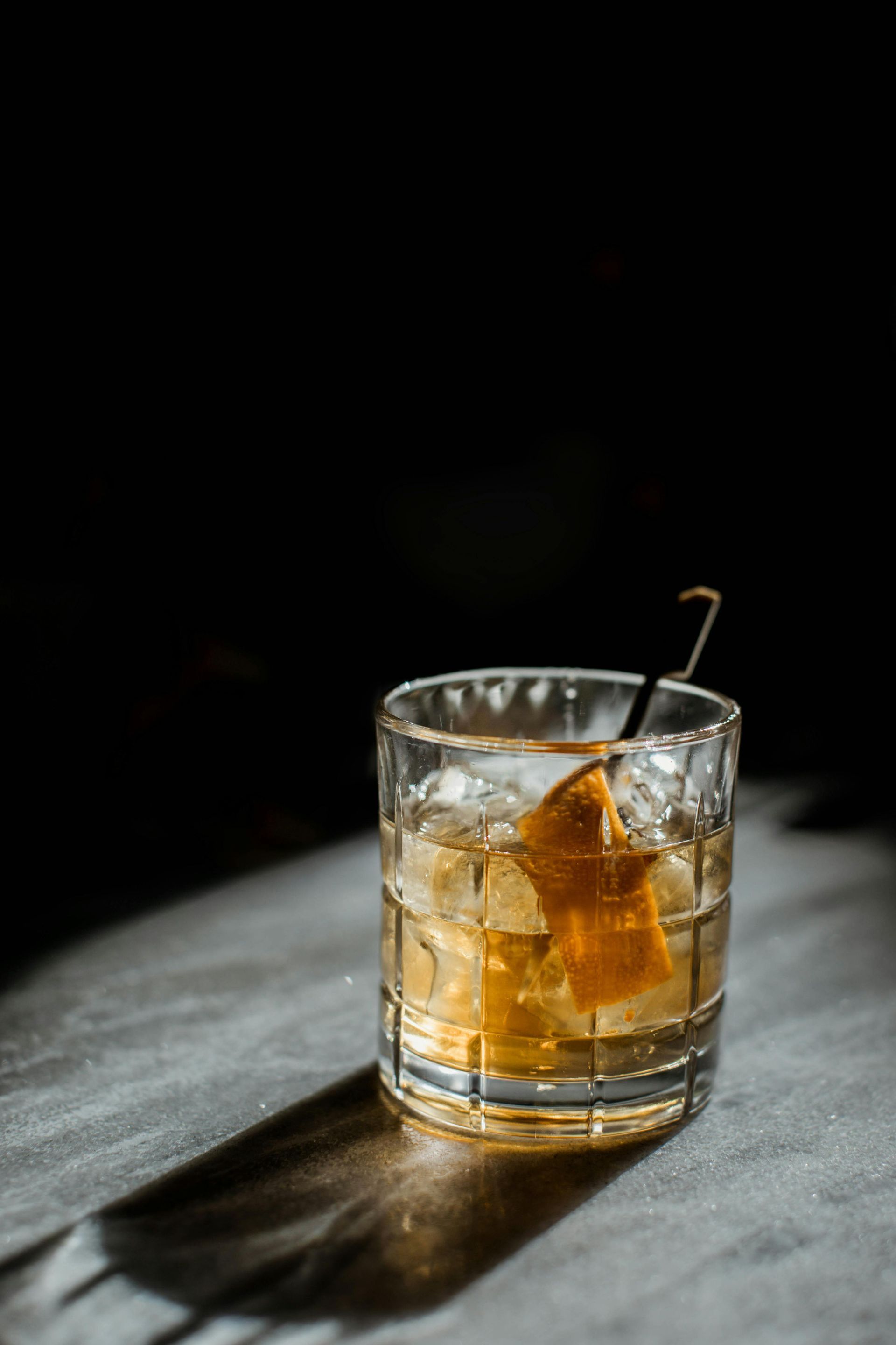 A glass of whiskey with ice and an orange peel on a table.