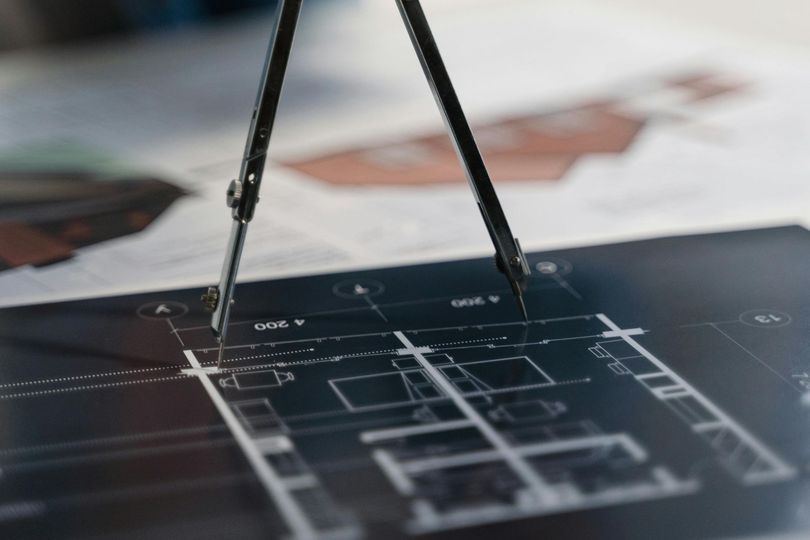 A person is using a compass to draw on a blueprint.