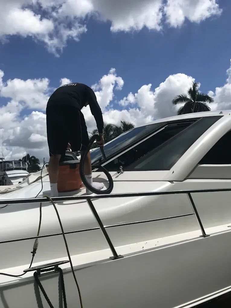 Person vacuuming the window of a white boat on a sunny day with puffy clouds.