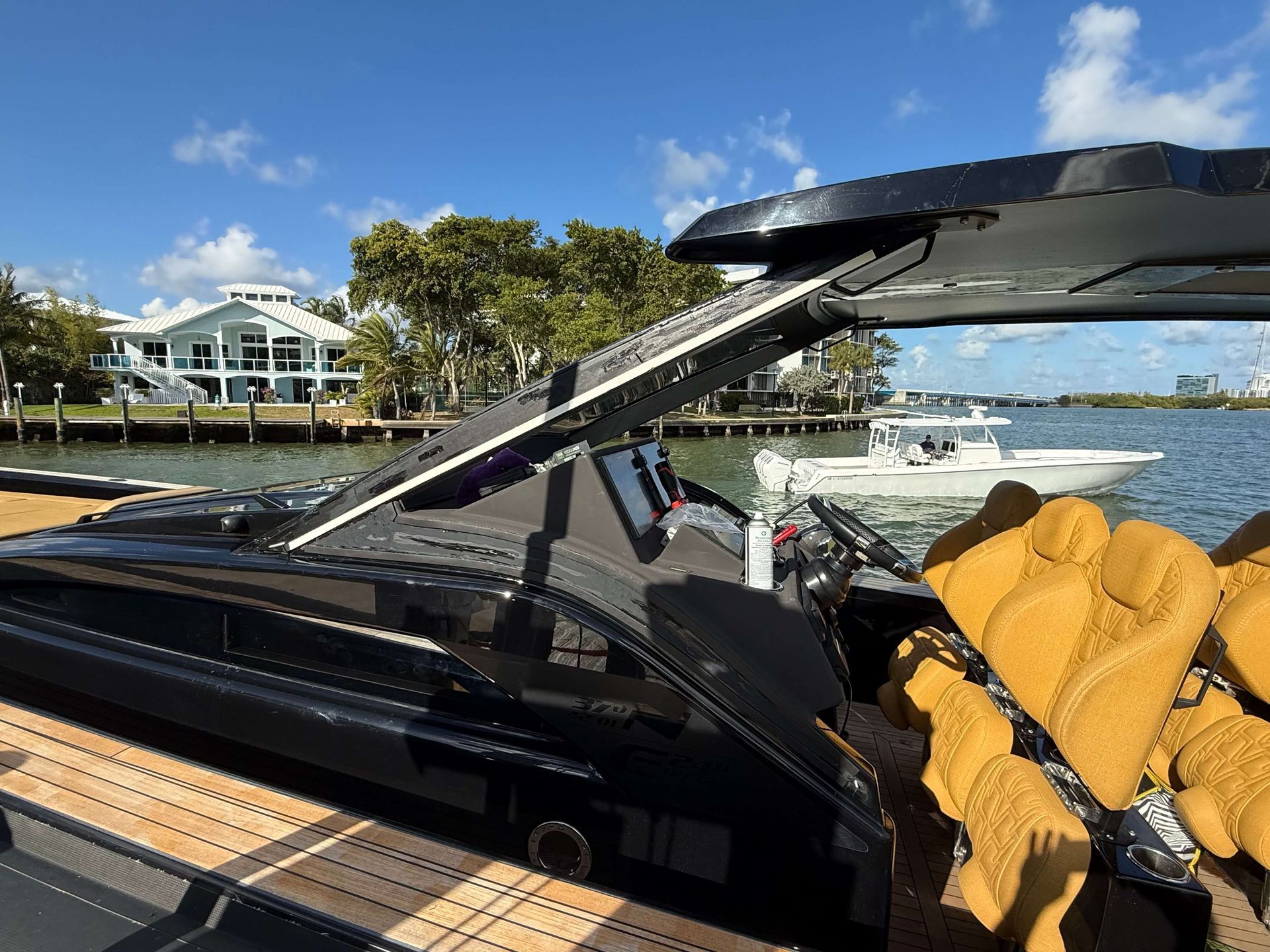 Person vacuums a boat's window, standing on the deck, blue sky with clouds in the background.
