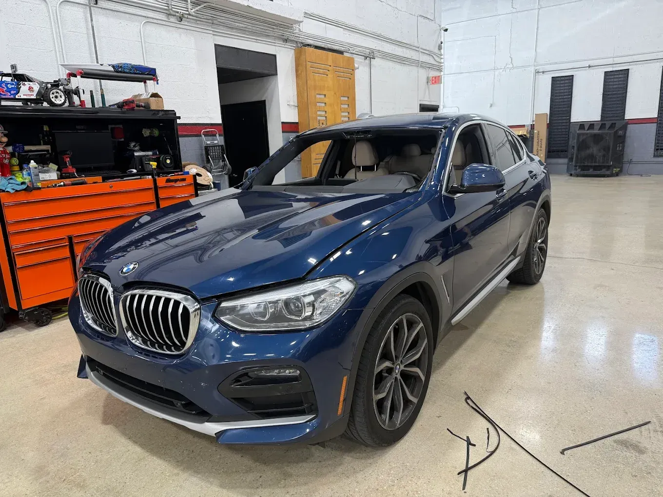 Blue BMW SUV in a garage, with toolboxes and open garage doors in the background.