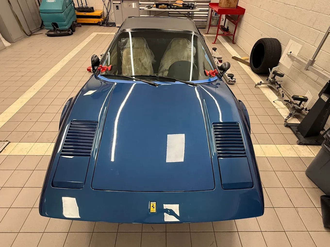Blue Ferrari 308 in a garage, seen from the front with the hood up.