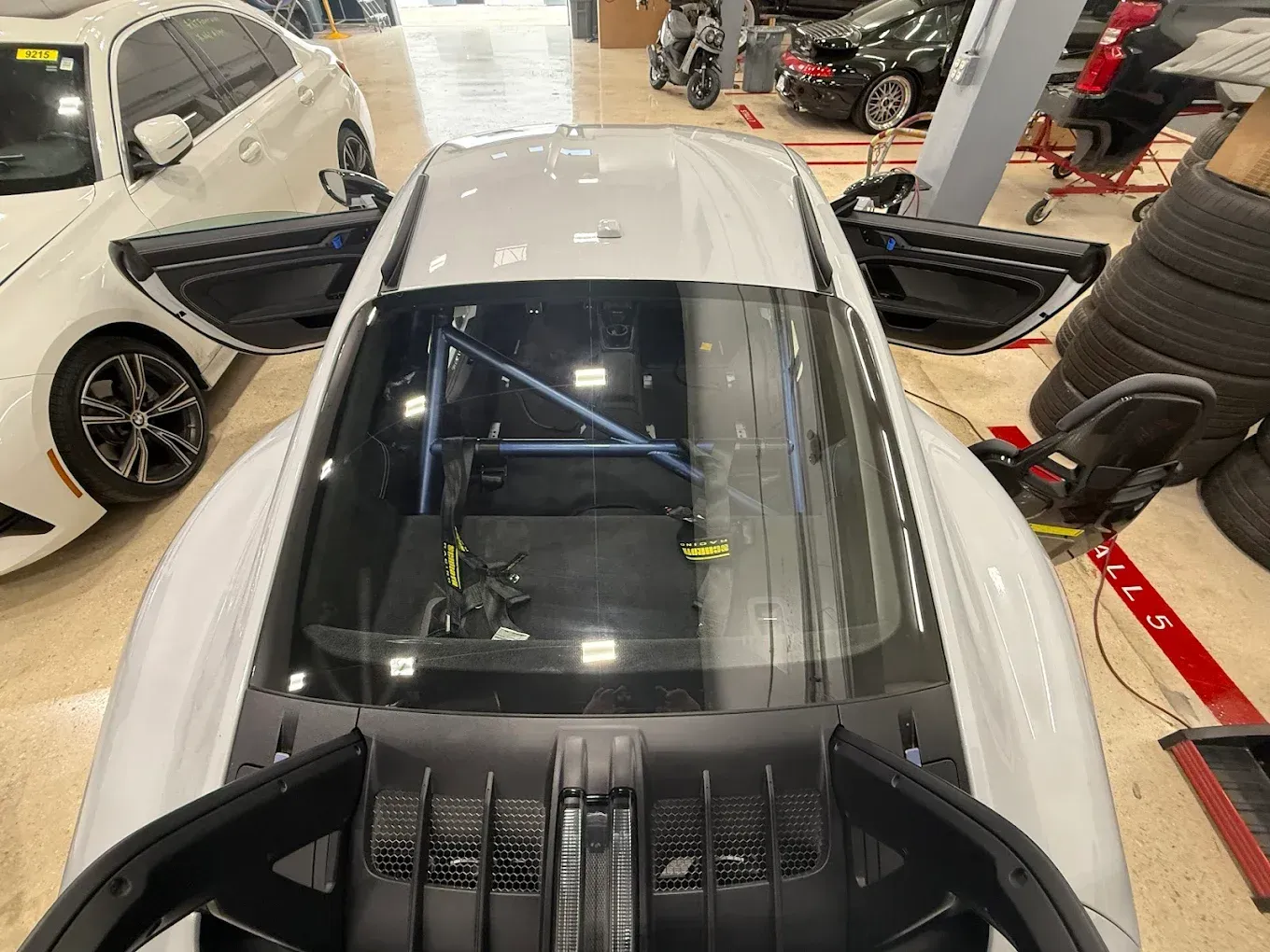 White sports car with open doors and roll cage inside a garage.