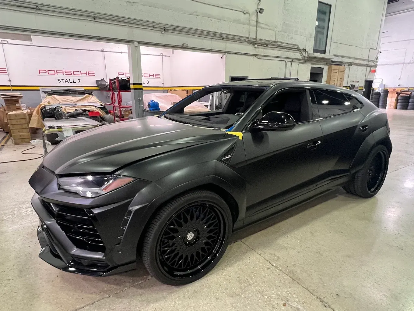 Black Lamborghini SUV in a workshop, black wheels, matte finish.
