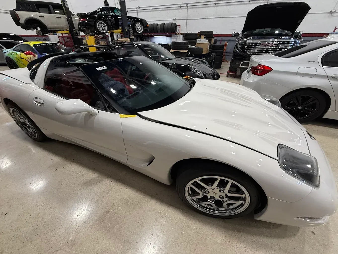 White Corvette in a garage, other vehicles in background.