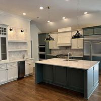 Modern kitchen with a large island, white countertops, and green and white cabinets, along with stainless steel appliances.