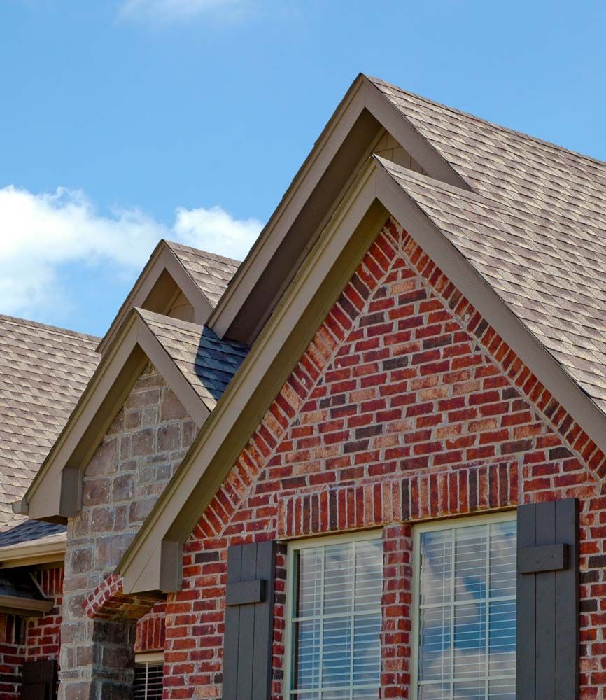 Brick house with gabled roof, brown shutters, and a blue sky.