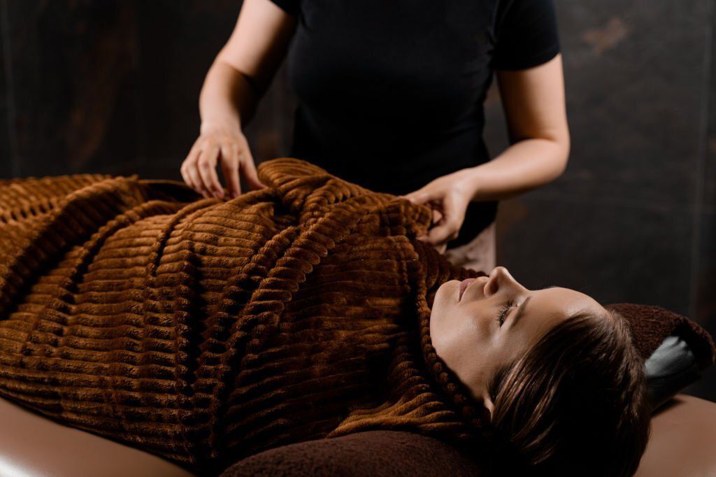 Full body wrap in warm blanket after chocolate massage beauty treatment for female model in spa