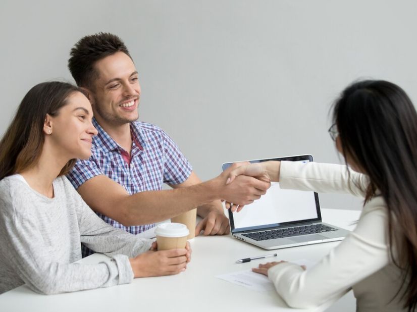 A man and woman are shaking hands with a woman while sitting at a table.