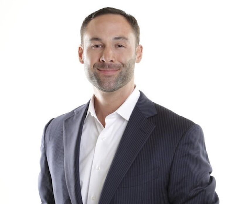 A man in a suit and white shirt is smiling for the camera.