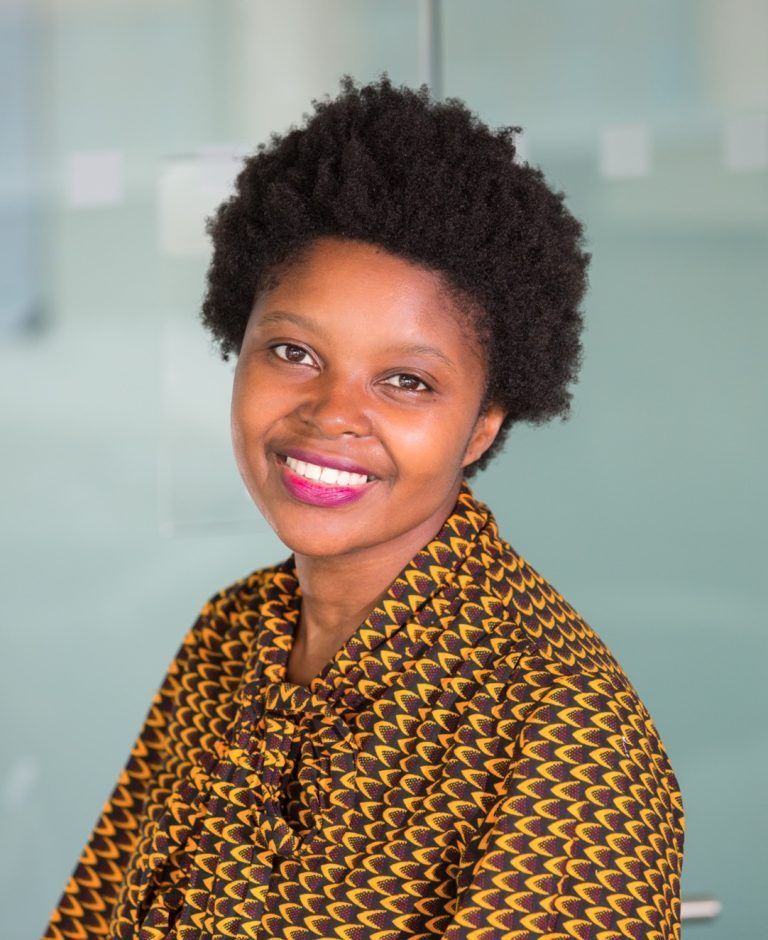 A woman in a yellow and brown shirt is smiling for the camera.