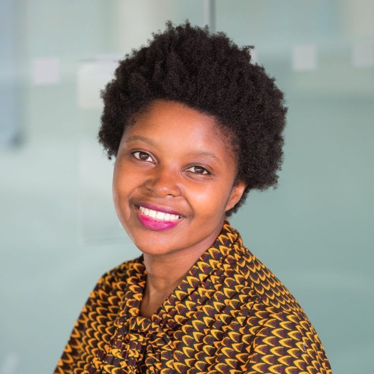 A woman wearing a yellow and brown shirt is smiling for the camera.