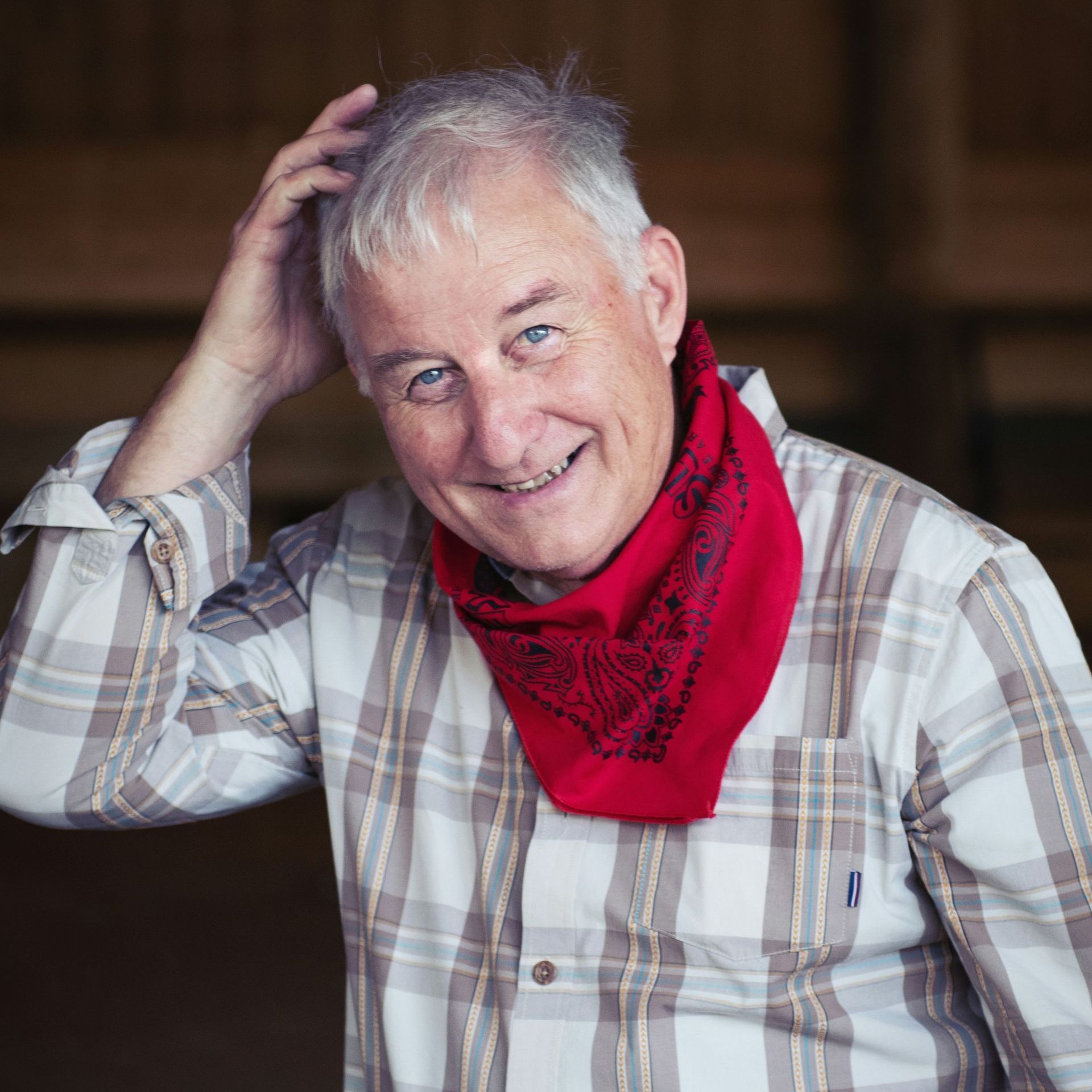 A man wearing a plaid shirt and a red bandana is smiling