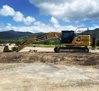 A Large Yellow Excavator Is Parked in A Dirt Field — Terranovus Earthworks & Plant Hire in Cairns, QLD