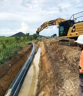 A Man Is Standing in A Trench Next to A Bulldozer — Terranovus Earthworks & Plant Hire in Cairns, QLD