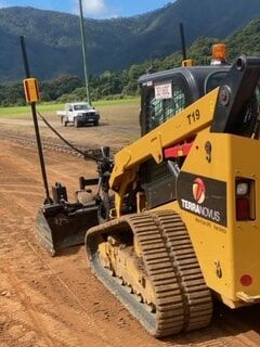A Yellow Bulldozer Is Parked in A Dirt Field with Mountains in The Background — Terranovus Earthworks & Plant Hire in Cairns, QLD