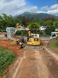 A Yellow Excavator Is Driving Down a Dirt Road — Terranovus Earthworks & Plant Hire in Cairns, QLD