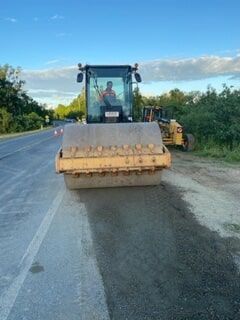 A Man Is Driving a Roller on The Side of A Road — Terranovus Earthworks & Plant Hire in Cairns, QLD