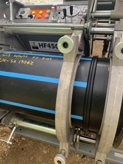 A Machine Is Cutting a Black Pipe with Blue Stripes — Terranovus Earthworks & Plant Hire in Cairns, QLD