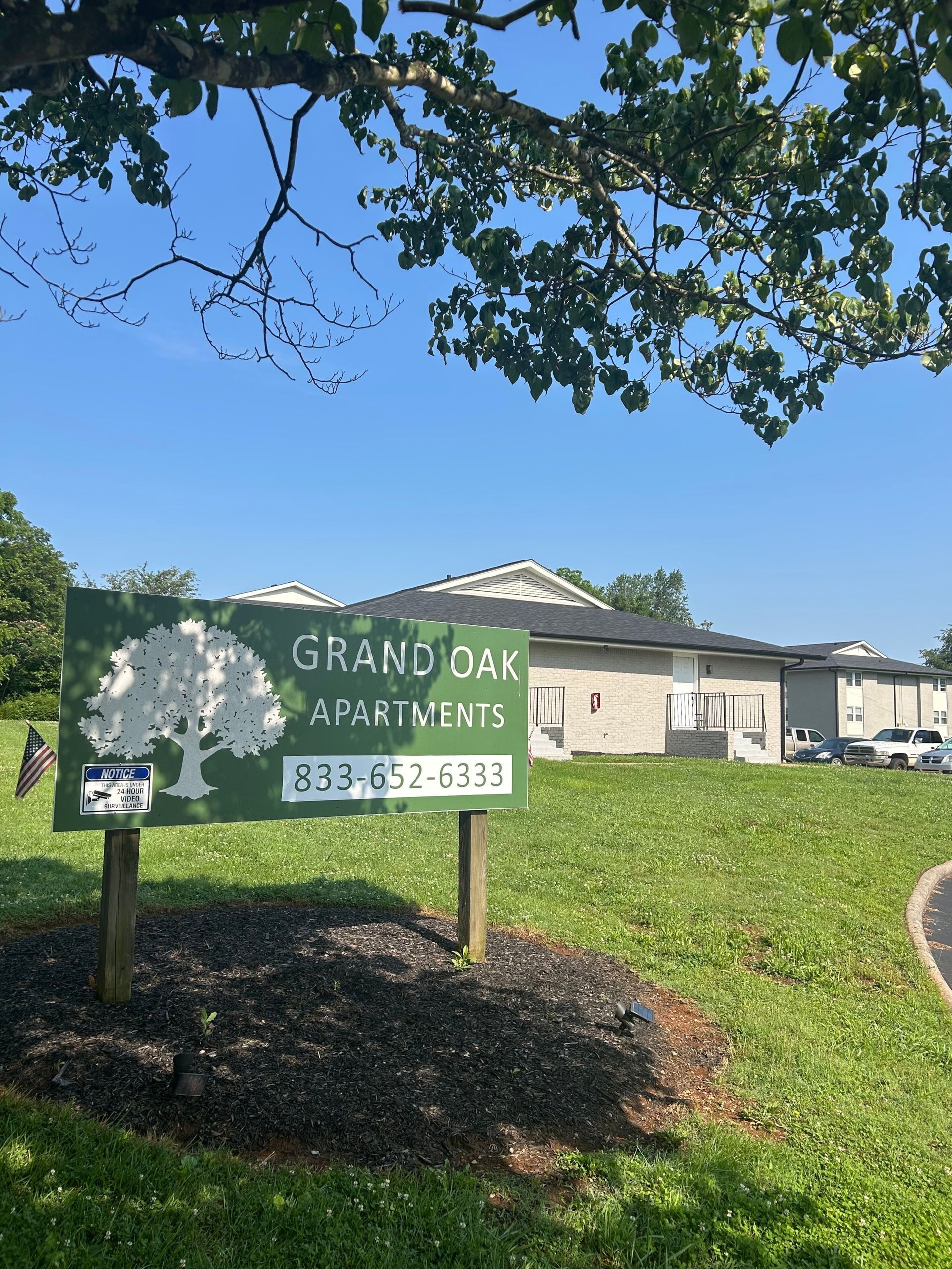 A sign for grand oak apartments is sitting in the middle of a grassy field.