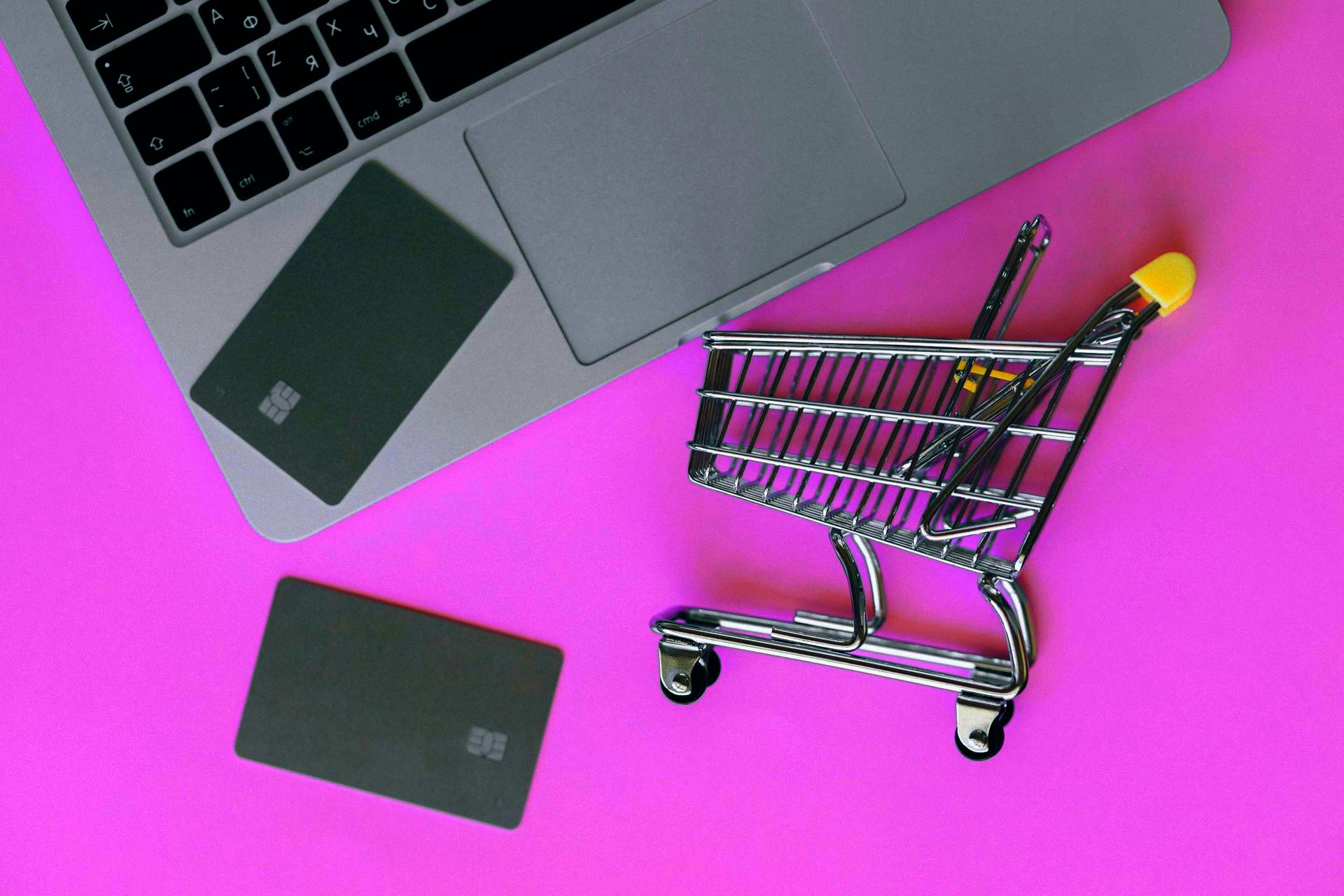 A shopping cart is sitting on top of a laptop next to a credit card.