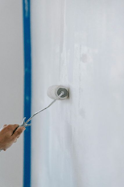 Person painting a white wall with a roller. Person painting a white wall with a roller.
