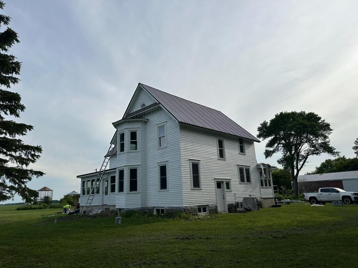 White two-story house with new striped roof, on a grassy field, under cloudy sky.