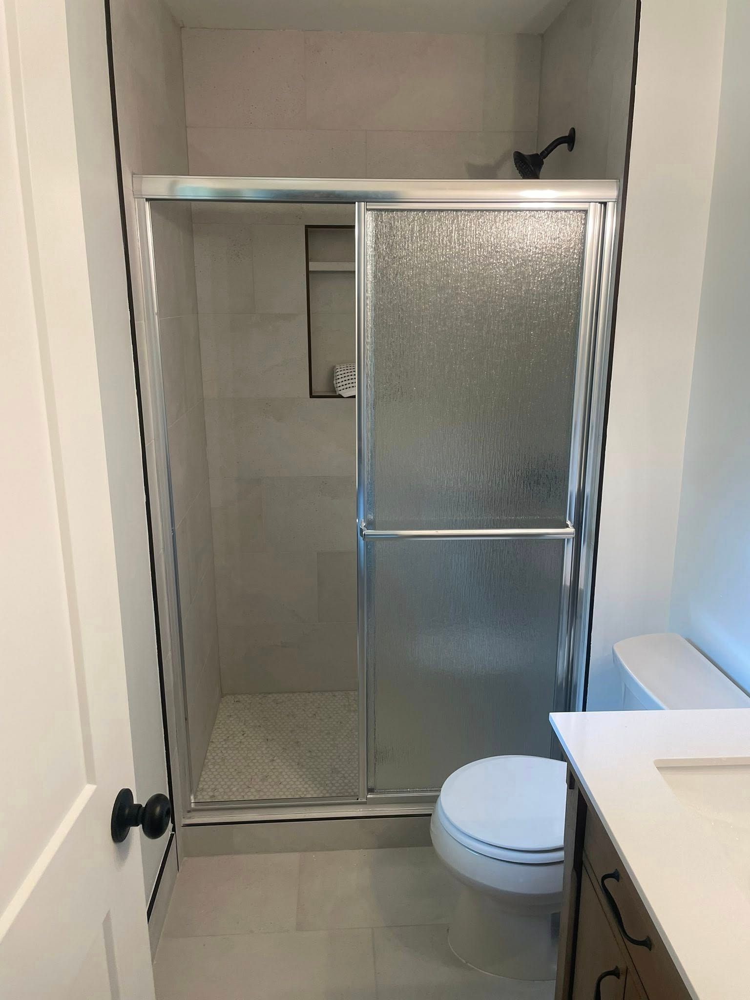Bathroom with shower and sliding glass door, toilet, and vanity. Neutral color scheme.