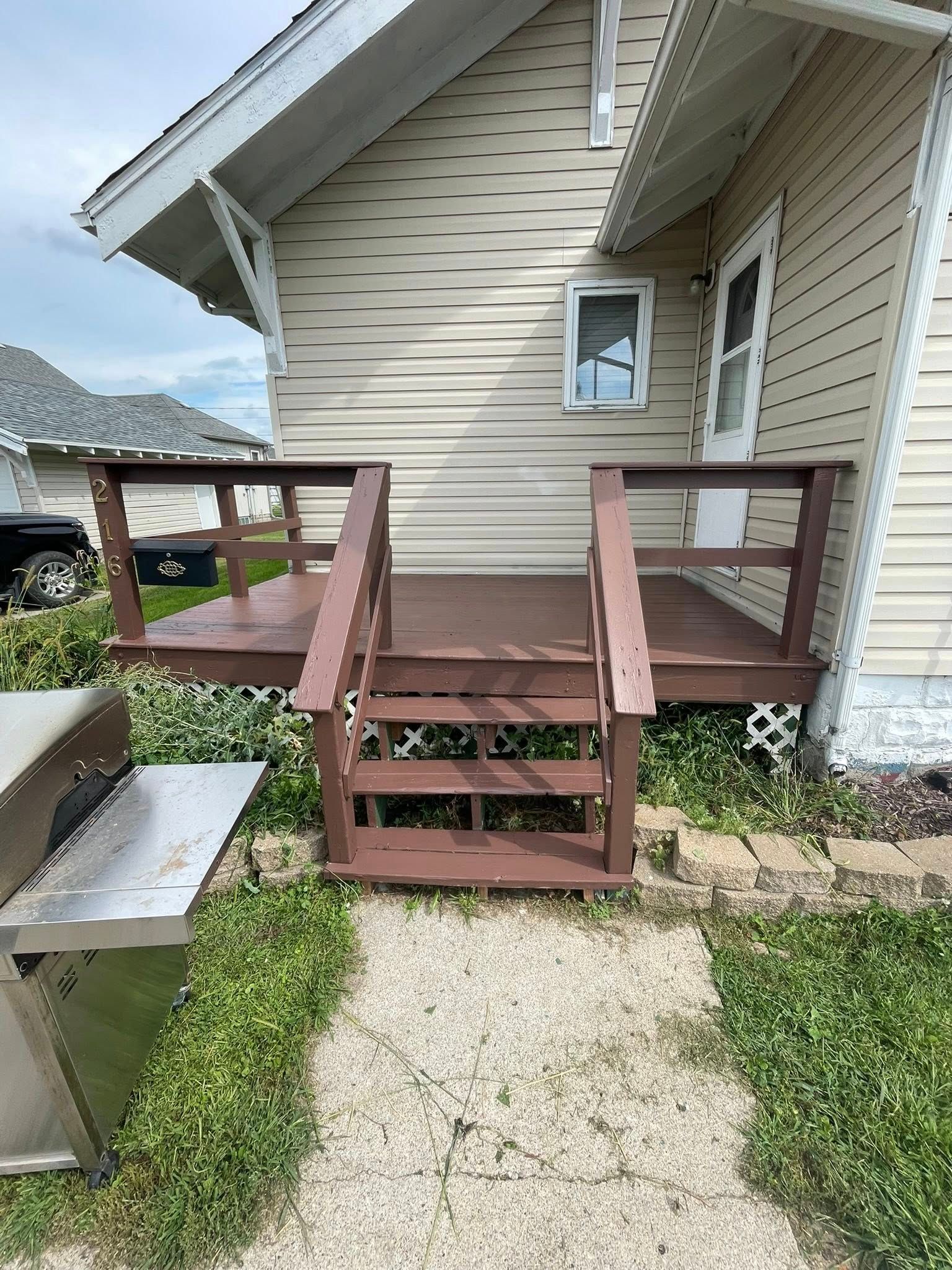 Wooden deck with stairs leading to a beige house with a small window.