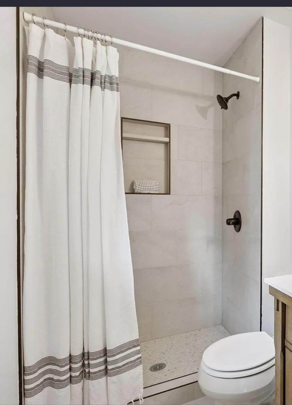 White-tiled shower with a clear glass side and white shower curtain. Features a niche and dark fixtures.