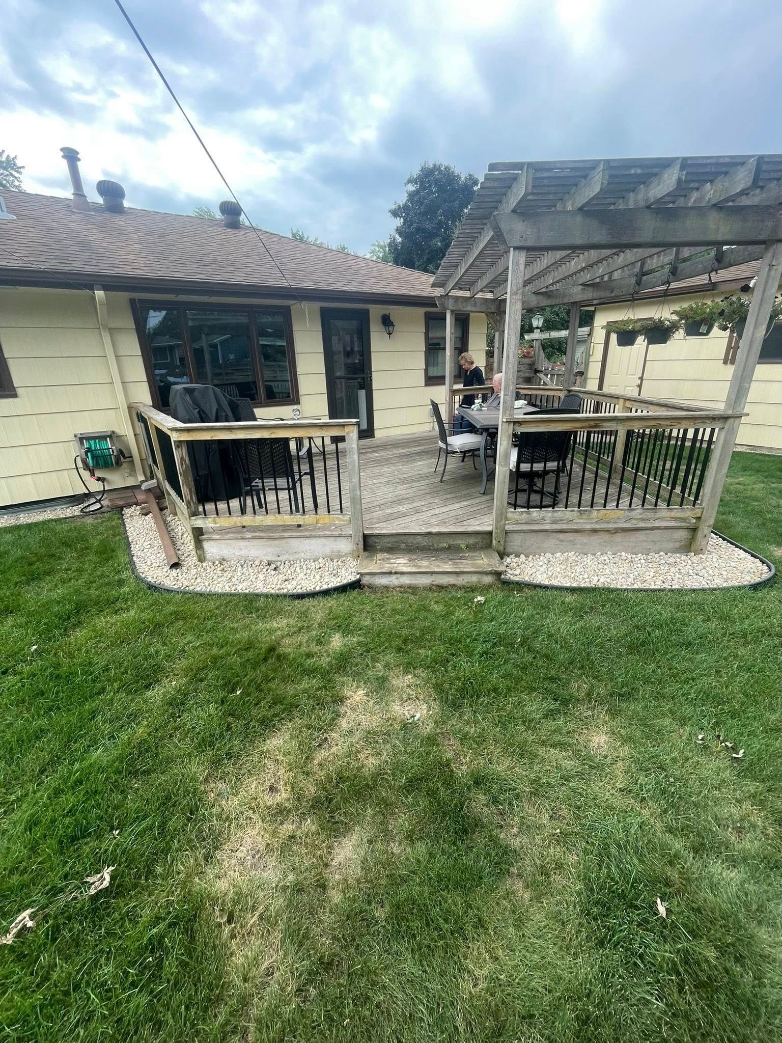 Backyard deck with pergola, gravel border, and patchy green lawn.