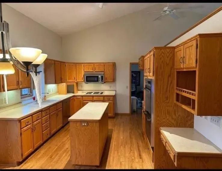 Kitchen with light wood cabinets, white countertops, island, and stainless steel appliances.