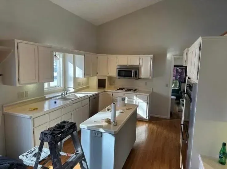 A white kitchen with countertops, cabinets, and island.  A ladder sits nearby.