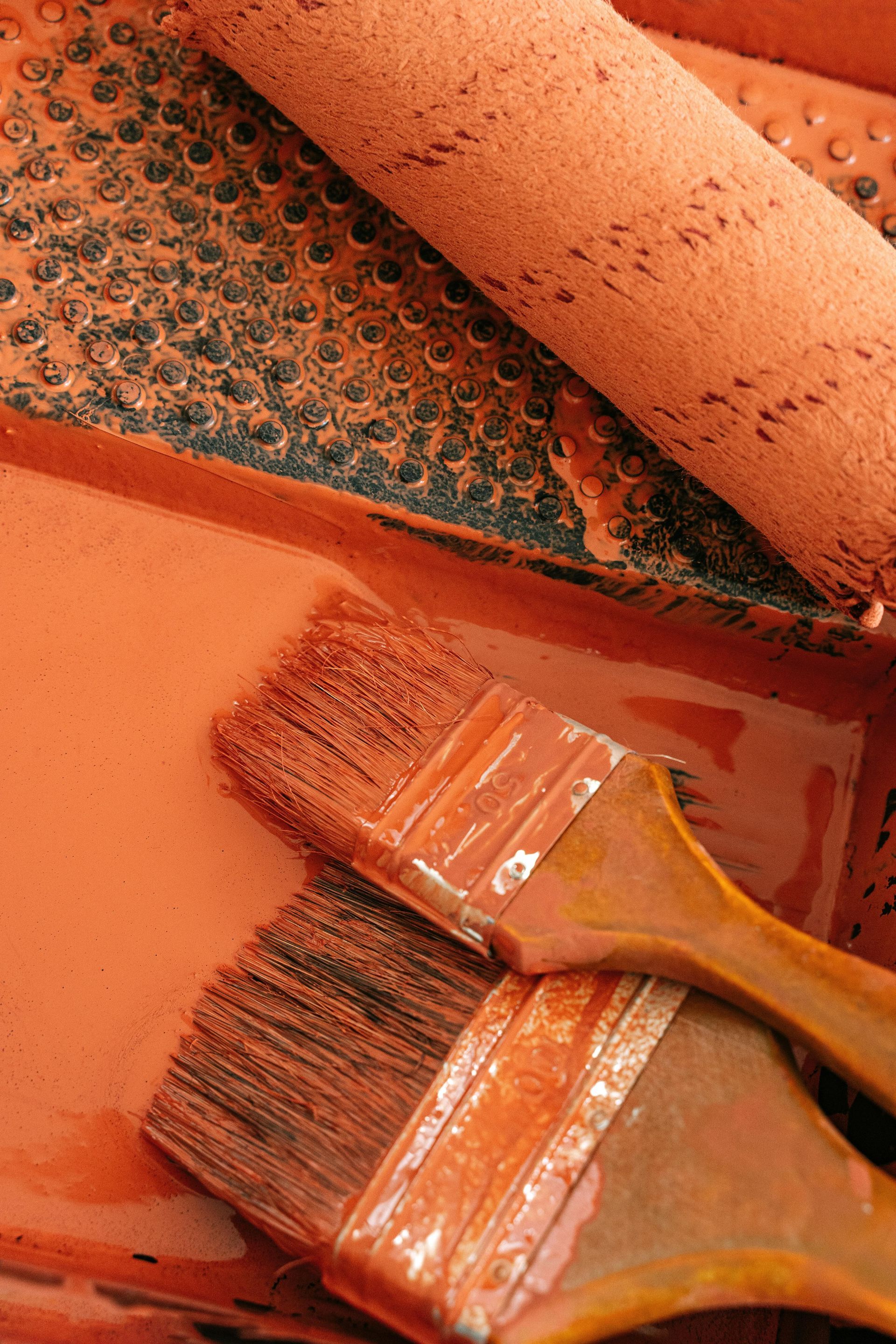 Paint tray with brushes and paint roller, all coated in orange paint.