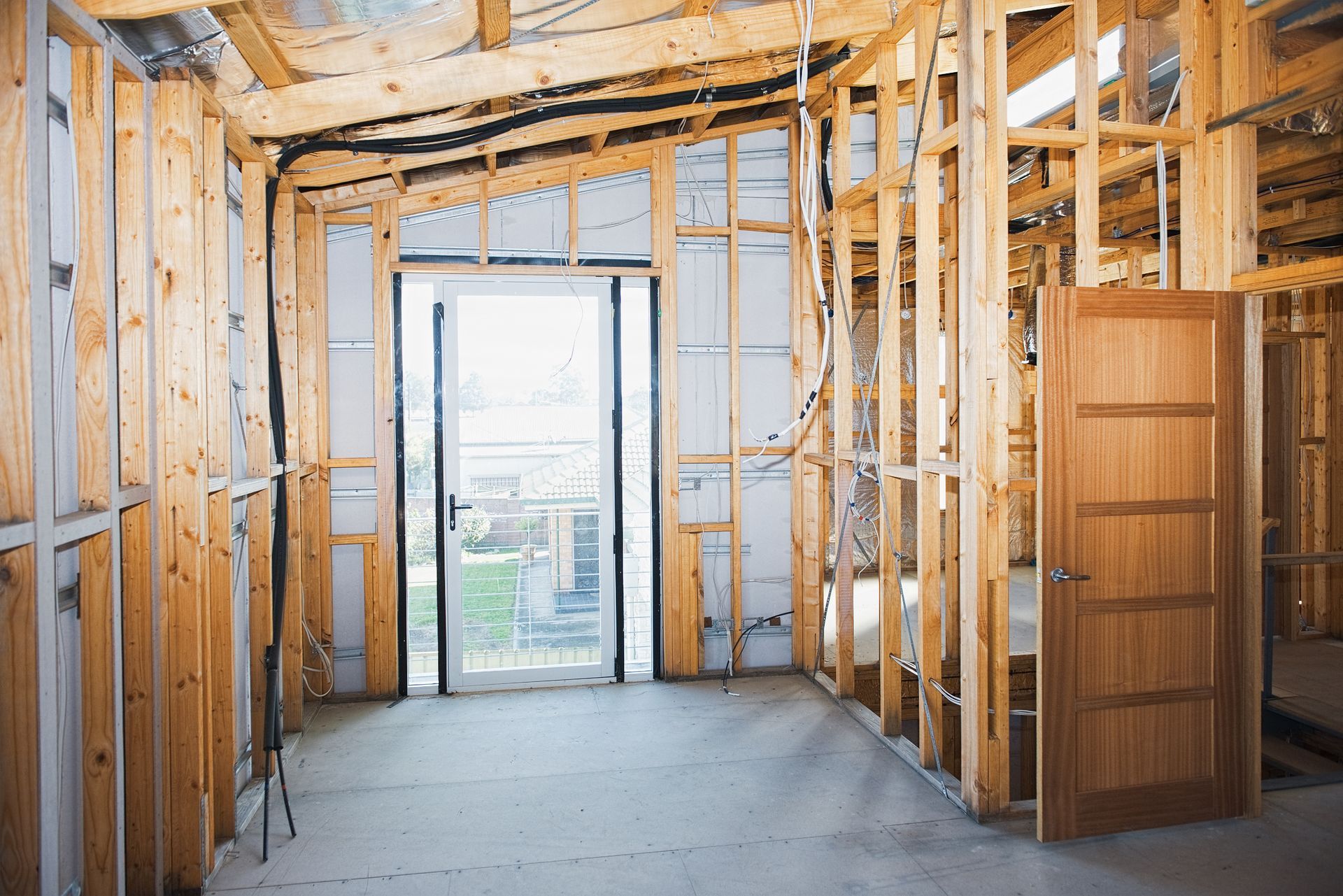 Interior construction with wooden framing and a closed door. Light streams through an open doorway.