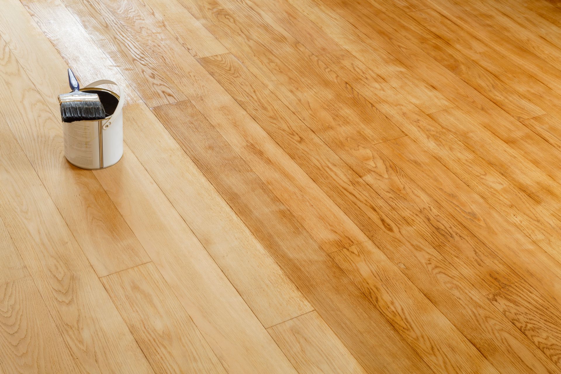 Wooden floor being refinished with varnish; a can and brush are visible.