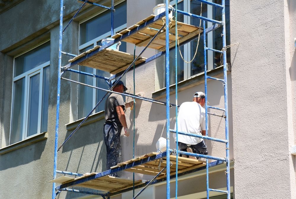 Two workers painting a building facade from a scaffold.