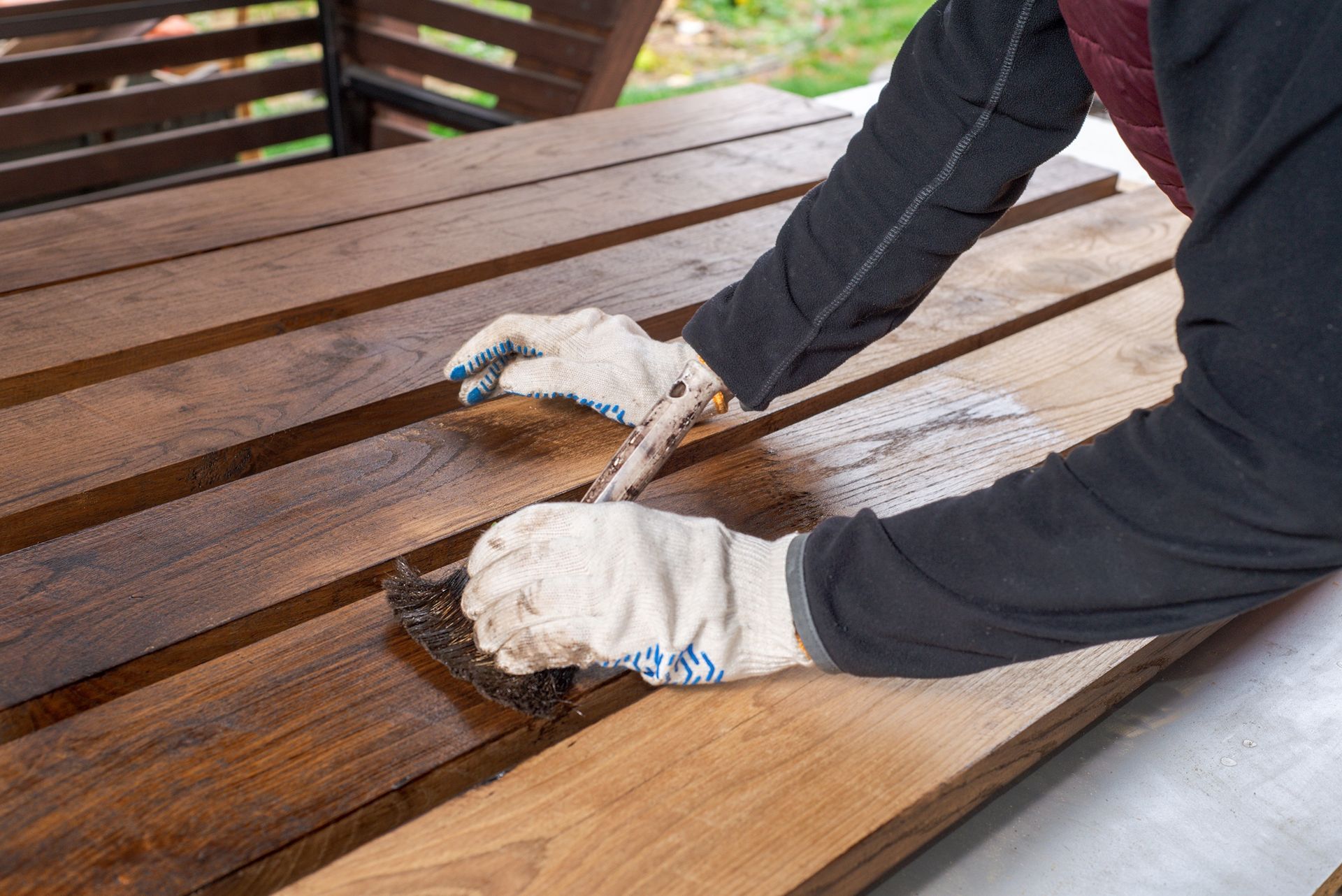 Person staining wooden planks on a table outdoors, wearing gloves.
