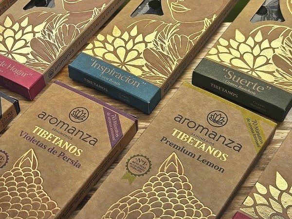 Cajas de incienso tibetano Aromanza en varios colores, con detalles dorados, sobre una superficie de madera.