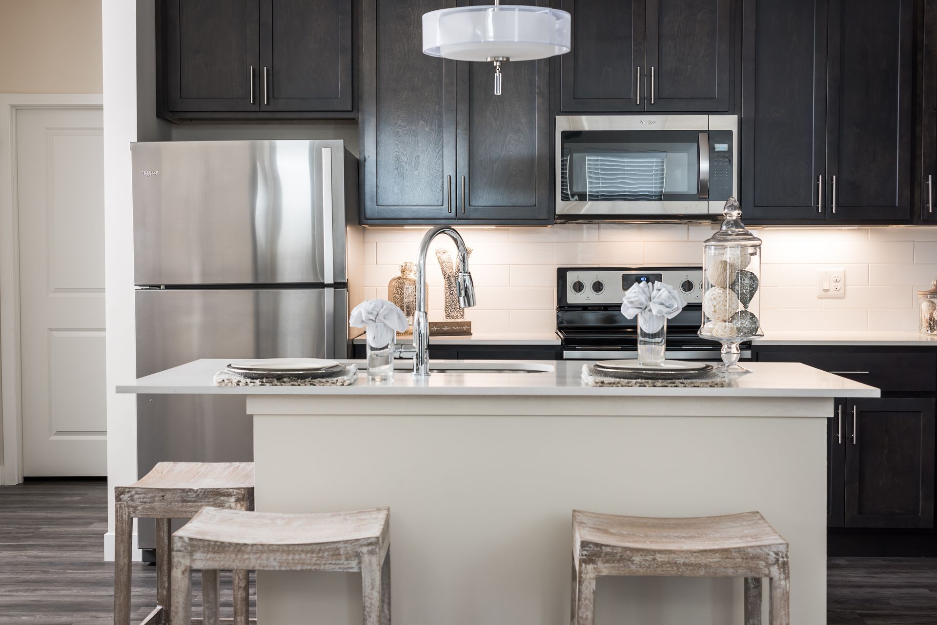 Modern kitchen with dark cabinets, stainless steel appliances, white island, stools, and white door.