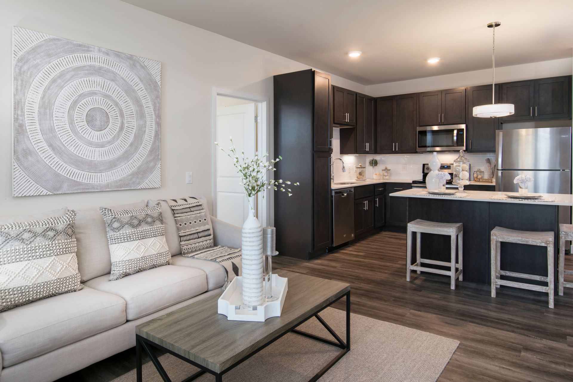 Living room and kitchen with sofa, art, dark cabinets, island with stools.