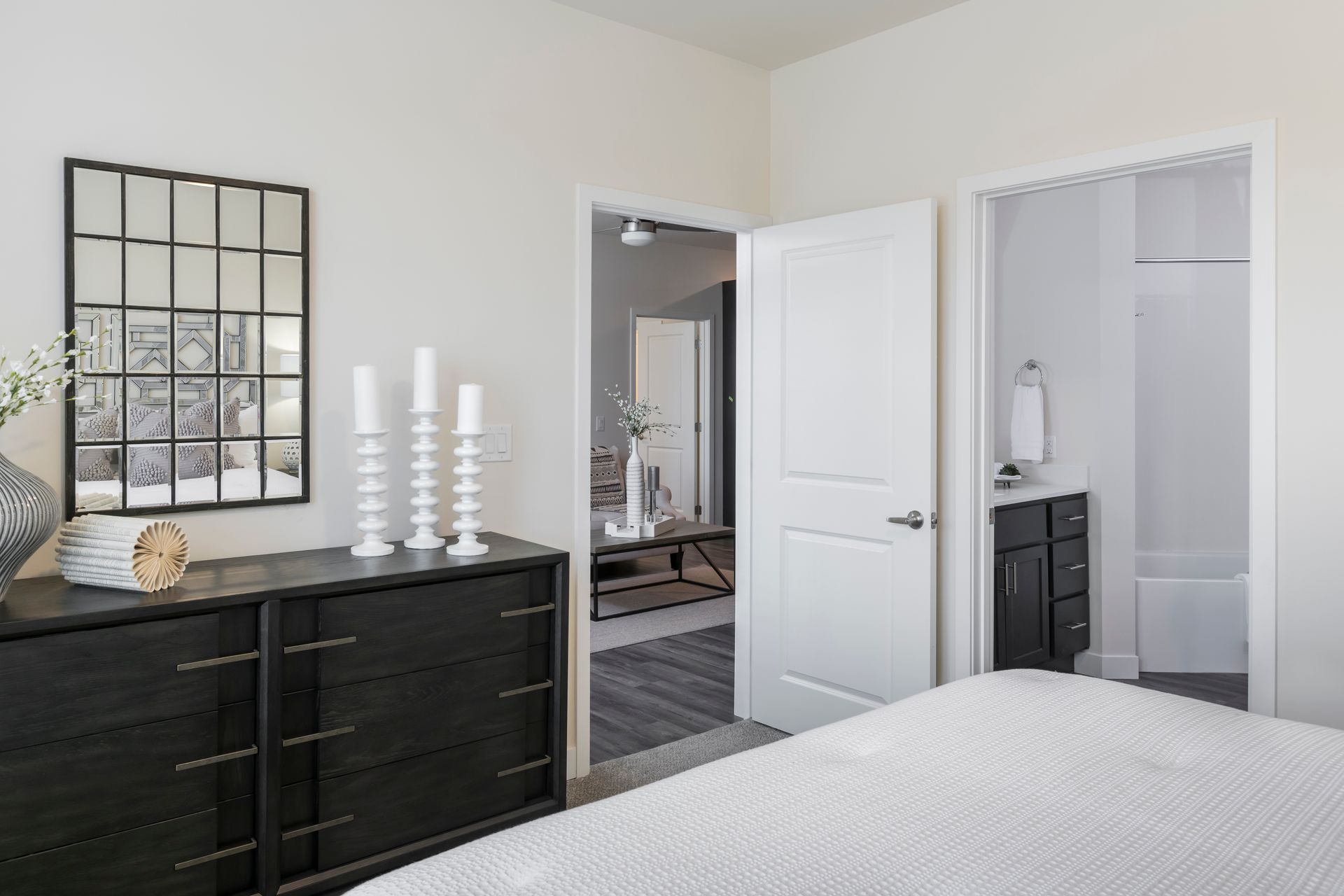 Bedroom with black dresser, white candles, mirror, and open doors to a bathroom and another room.