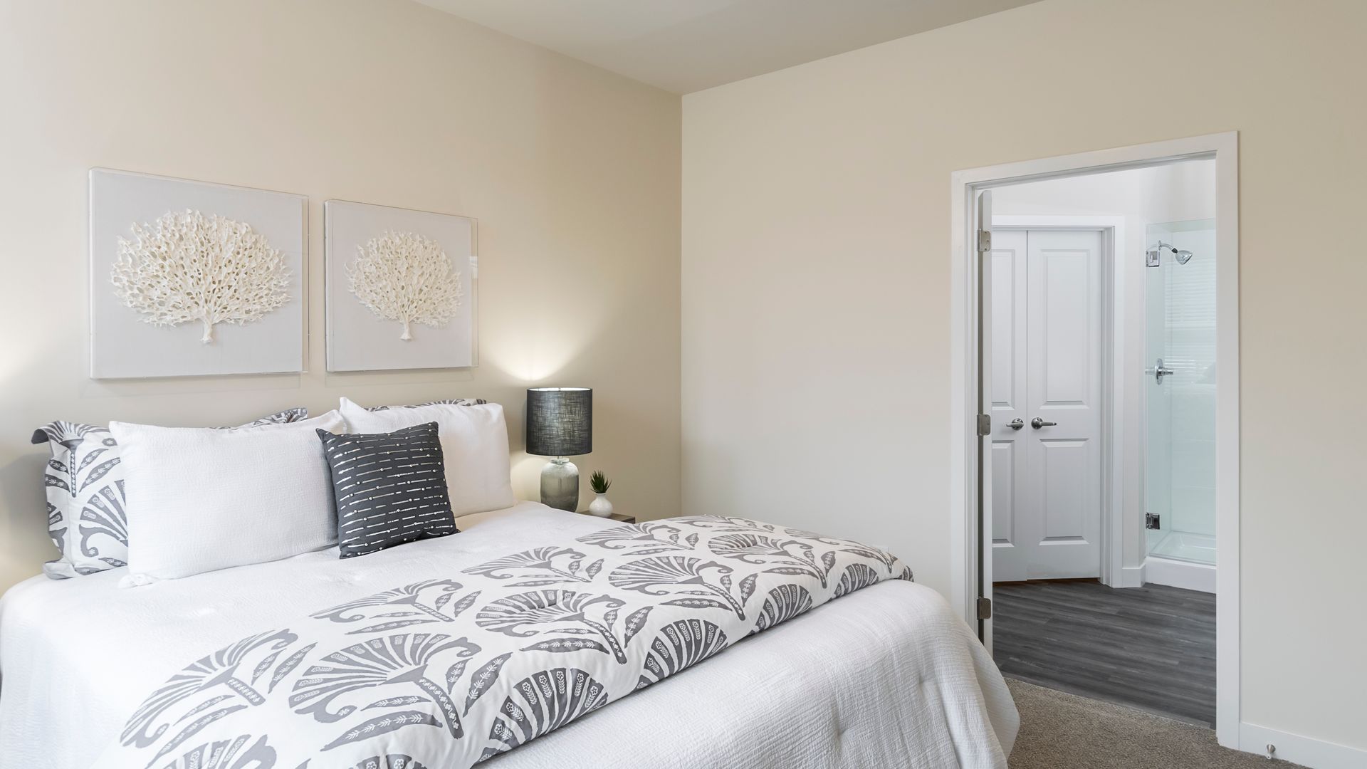 Bedroom with a bed, two framed artworks, and an open doorway to a bathroom. The room is light-colored.
