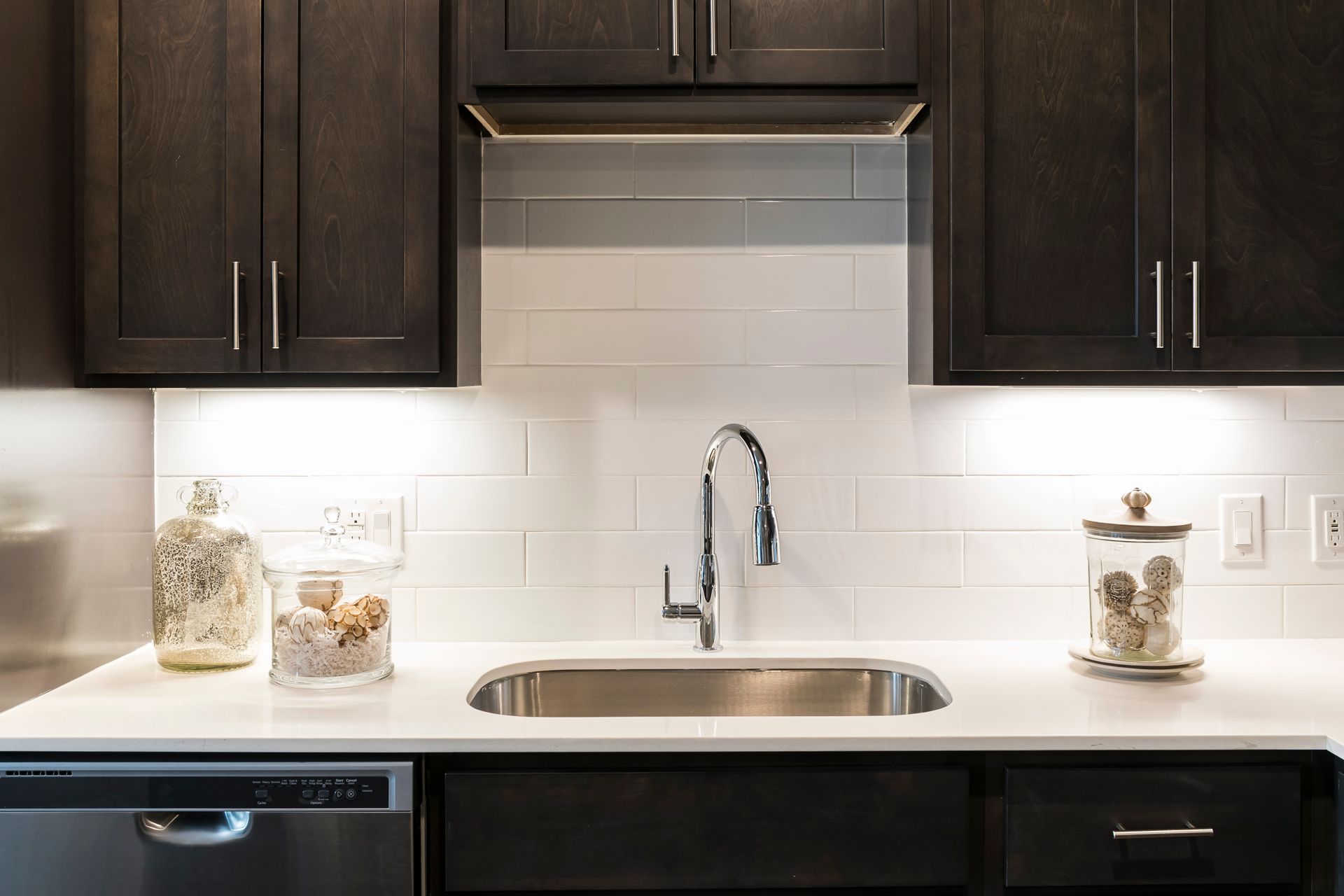 Modern kitchen with dark wood cabinets, white countertops, stainless steel sink, and white subway tile backsplash.
