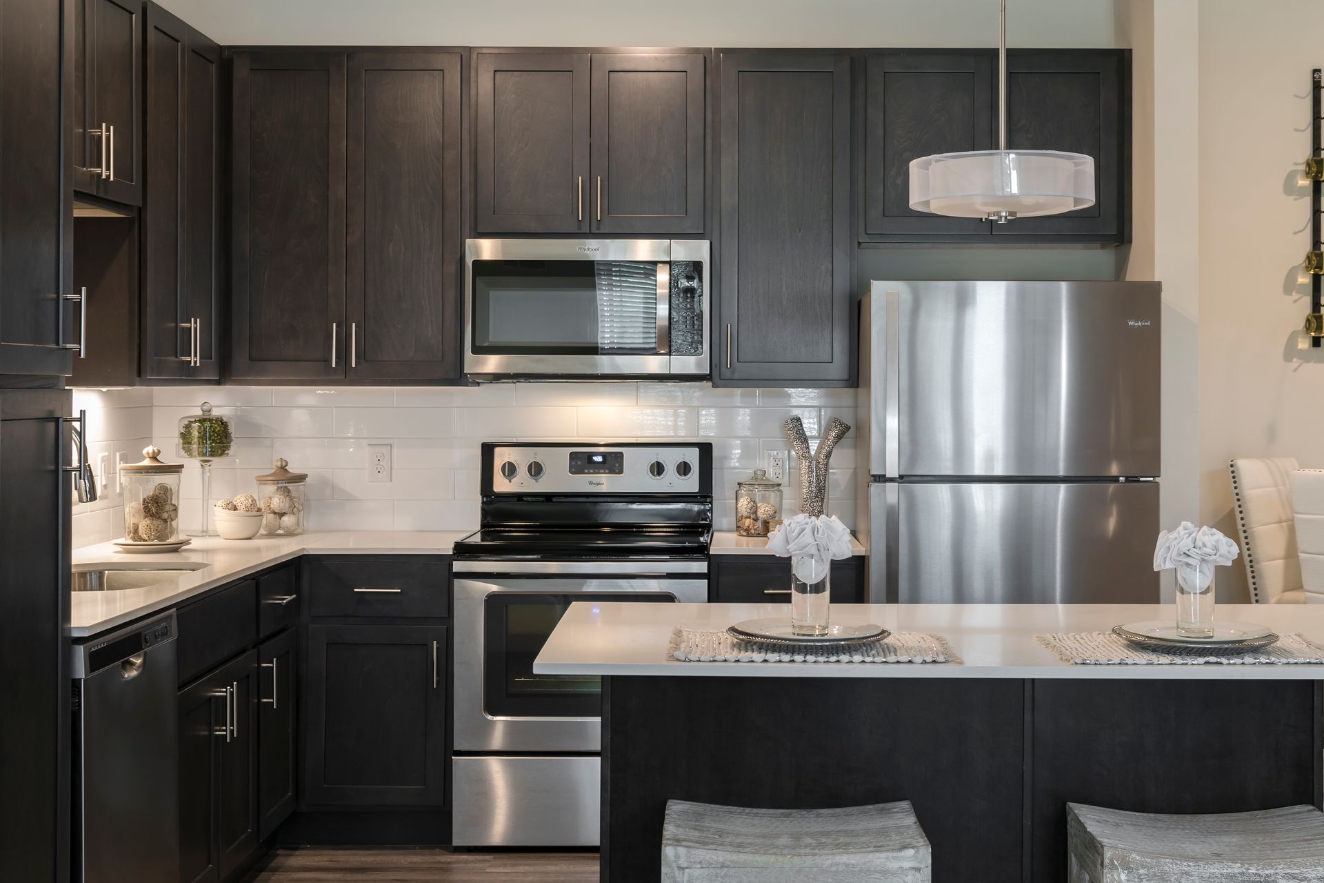Modern kitchen with dark cabinets, stainless steel appliances, and a white countertop island.